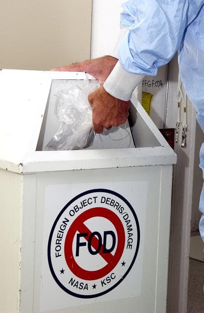NASA image: KENNEDY SPACE CENTER, FLA. -  A KSC employee dressed in a "bunny suit," standard clean room apparel, disposes of some waste material into a container designated for the purpose. The apparel is designed to cover the hair, clothing and shoes of employees entering a clean room to prevent particulate matter from contaminating the space flight hardware being stored or processed in the room. The suit and container are both part of KSC's Foreign Object Debris (FOD) control program, an important safety initiative.
