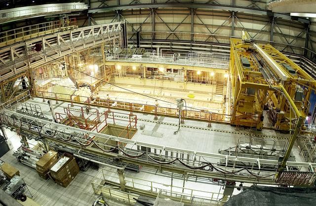 NASA image: KENNEDY SPACE CENTER, FLA. -  This bird's-eye view of a high bay in the Orbiter Processing Facility (OPF) shows the open payload bay of Space Shuttle Discovery surrounded by the standard platforms and equipment required to process a Space Shuttle orbiter.  The high bay is 197 feet (60 meters) long, 150 feet (46 meters) wide, 95 feet (29 meters) high, and encompasses a 29,000-square-foot (2,694-meter) area.  The 30-ton (27-metric-ton) bridge crane (yellow device, right) has a hook height of approximately 66 feet (20 meters).  Platforms, a main access bridge, and two rolling bridges with trucks provide access to various parts of the orbiter.  In addition to routine servicing and checkout, the inspections and modifications made to enhance Discovery's performance and upgrade its systems were performed in the OPF during its recently completed Orbiter Major Modification (OMM) period.