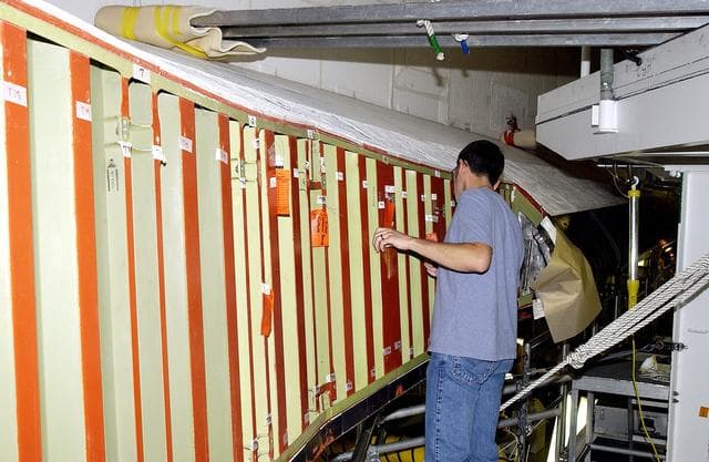 NASA image: KENNEDY SPACE CENTER, FLA. - In the Orbiter Processing Facility (OPF), a United Space Alliance technician examines the attachment points for the spars on the exterior of a wing of Space Shuttle Atlantis. Reinforced Carbon Carbon (RCC) panels are mechanically attached to the wing with a series of floating joints - spars - to reduce loading on the panels caused by wing deflections. The aluminum and the metallic attachments are protected from exceeding temperature limits by internal insulation.  The next launch of Atlantis will be on mission STS-114, a utilization and logistics flight to the International Space Station.