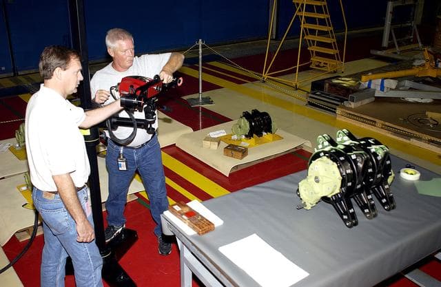 NASA image: KENNEDY SPACE CENTER, FLA. -   Boeing workers get ready to perform a 3D digital scan of the actuator on the table.  At left is John Macke, from Boeing, St. Louis.   At right is Dan Clark.. There are two actuators per engine on the Shuttle, one for pitch motion and one for yaw motion. The Space Shuttle Main Engine hydraulic servoactuators are used to gimbal the main engine.