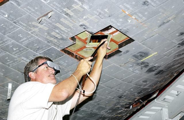 NASA image: KENNEDY SPACE CENTER, FLA. -  In the Orbiter Processing Facility, Greg Harlow, with United Space Alliance (USA), threads a camera under the tiles of the orbiter Endeavour to inspect for corrosion.