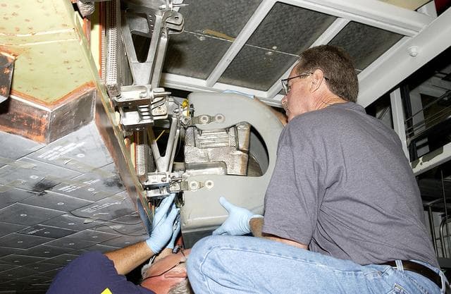 NASA image: KENNEDY SPACE CENTER, FLA. -  In the Orbiter Processing Facility, United Space Alliance worker Mike Hyatt (right) attaches a Reinforced Carbon Carbon (RCC) panel onto the leading edge of the wing of the orbiter Atlantis.  The gray carbon composite RCC panels have sufficient strength to withstand the aerodynamic forces experienced during launch and reentry, which can reach as high as 800 pounds per square foot. The operating range of RCC is from minus 250º F to about 3,000º F, the temperature produced by friction with the atmosphere during reentry.