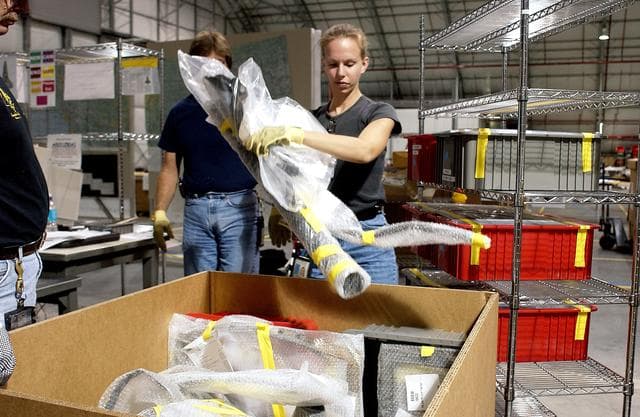 NASA image: KENNEDY SPACE CENTER, FLA. - James Harrison (left), Jack Nowling (center) and Amy Norris (right) pack up some of the debris stored in the Columbia Debris Hangar.  About 83,000 pieces were shipped to KSC during search and recovery efforts in East Texas. An area of the Vehicle Assembly Building is being prepared to store the debris.