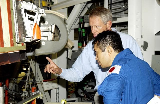 NASA image: KENNEDY SPACE CENTER, FLA. - Japanese astronaut Koichi Wakata (front) listens to William Gaetjens, with the Vehicle Integration Test Team (VITT), who is providing details about the spar installation (left) on the wing of the orbiter Atlantis.  Reinforced Carbon Carbon (RCC) panels are mechanically attached to the wing via the spars - a series of floating joints - to reduce loading on the panels caused by wing deflections. The aluminum and the metallic attachments are protected from exceeding temperature limits by internal insulation.
