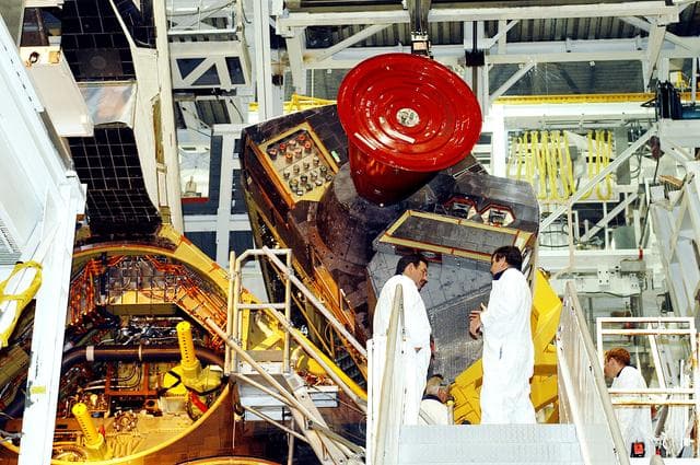 NASA image: KENNEDY SPACE CENTER, FLA. -   Technicians in the Orbiter Processing Facility oversee removal of one of two orbital maneuvering system (OMS) pods from Endeavour.  The OMS pods are attached to the upper aft fuselage left and right sides.  Fabricated primarily of graphite epoxy composite and aluminum, each pod is 21.8 feet long and 11.37 feet wide at its aft end and 8.41 feet wide at its forward end, with a surface area of approximately 435 square feet.  Each pod houses the Reaction Control System propulsion components used for inflight maneuvering and is attached to the aft fuselage with 11 bolts.   OMS pods are removed during Orbiter Major Modifications. Once removed, the OMS pods undergo in-depth structural inspections, system checks and the thrusters are changed out.