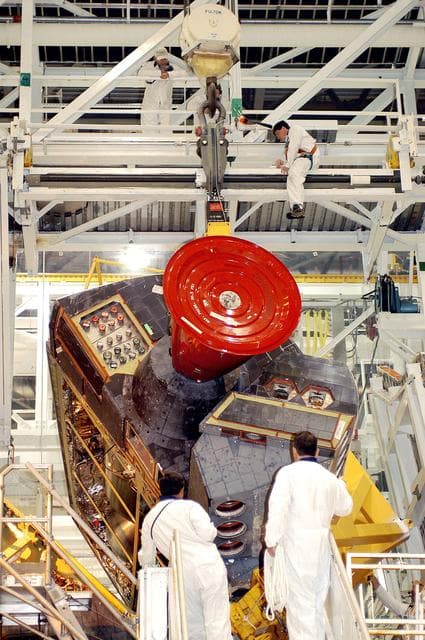 NASA image: KENNEDY SPACE CENTER, FLA. -   Technicians in the Orbiter Processing Facility oversee removal of one of two orbital maneuvering system (OMS) pods from Endeavour.  The OMS pods are attached to the upper aft fuselage left and right sides.  Fabricated primarily of graphite epoxy composite and aluminum, each pod is 21.8 feet long and 11.37 feet wide at its aft end and 8.41 feet wide at its forward end, with a surface area of approximately 435 square feet.  Each pod houses the Reaction Control System propulsion components used for inflight maneuvering and is attached to the aft fuselage with 11 bolts.   OMS pods are removed during Orbiter Major Modifications. Once removed, the OMS pods undergo in-depth structural inspections, system checks and the thrusters are changed out.