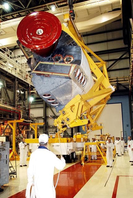 NASA image: KENNEDY SPACE CENTER, FLA. -  In the Orbiter Processing Facility, one of two orbital maneuvering system (OMS) pods removed from Endeavour is lowered toward a transporter.  The OMS pods are attached to the upper aft fuselage left and right sides.  Fabricated primarily of graphite epoxy composite and aluminum, each pod is 21.8 feet long and 11.37 feet wide at its aft end and 8.41 feet wide at its forward end, with a surface area of approximately 435 square feet.  Each pod houses the Reaction Control System propulsion components used for inflight maneuvering and is attached to the aft fuselage with 11 bolts.   OMS pods are removed during Orbiter Major Modifications. Once removed, the OMS pods undergo in-depth structural inspections, system checks and the thrusters are changed out.
