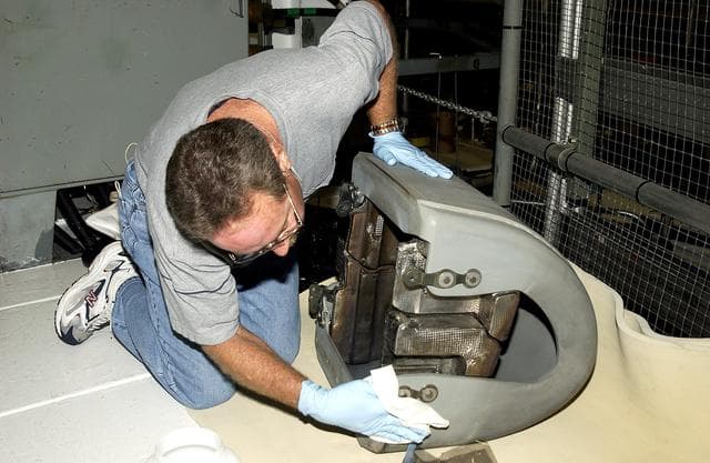 NASA image: KENNEDY SPACE CENTER, FLA. -  In the Orbiter Processing Facility, United Space Alliance worker Mike Hyatt looks over a Reinforced Carbon Carbon (RCC) panel that will be attached to the leading edge of the wing of the orbiter Atlantis.  The gray carbon composite RCC panels have sufficient strength to withstand the aerodynamic forces experienced during launch and reentry, which can reach as high as 800 pounds per square foot.  The operating range of RCC is from minus 250º F to about 3,000º F, the temperature produced by friction with the atmosphere during reentry.