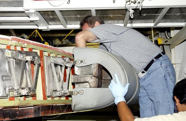 NASA image: KENNEDY SPACE CENTER, FLA. - In the Orbiter Processing Facility, United Space Alliance workers Mike Hyatt (above) and Saul Ngy (below right) finish installing a Reinforced Carbon Carbon (RCC) panel to the leading edge of the wing of the orbiter Atlantis.  The gray carbon composite RCC panels have sufficient strength to withstand the aerodynamic forces experienced during launch and reentry, which can reach as high as 800 pounds per square foot.  The operating range of RCC is from minus 250º F to about 3,000º F, the temperature produced by friction with the atmosphere during reentry.