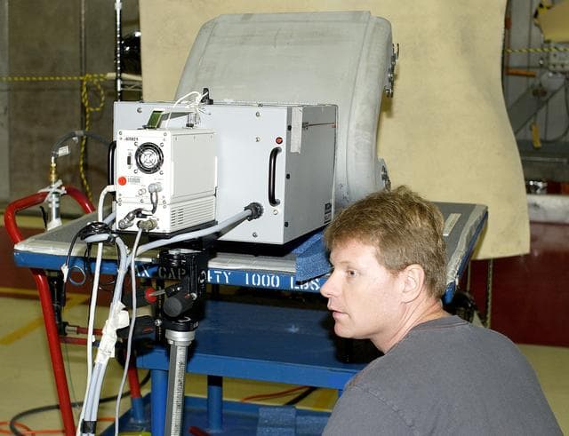 NASA image: KENNEDY SPACE CENTER, FLA. - In the Orbiter Processing Facility,  Jim Landy, NDE specialist with United Space Alliance (USA), watches a monitor off-screen to examine a Reinforced Carbon Carbon panel using flash thermography.  Attached to the leading edge of the wing of the orbiters,  the gray carbon composite RCC panels have sufficient strength to withstand the aerodynamic forces experienced during launch and reentry, which can reach as high as 800 pounds per square foot.  The operating range of RCC is from minus 250º F to about 3,000º F, the temperature produced by friction with the atmosphere during reentry.