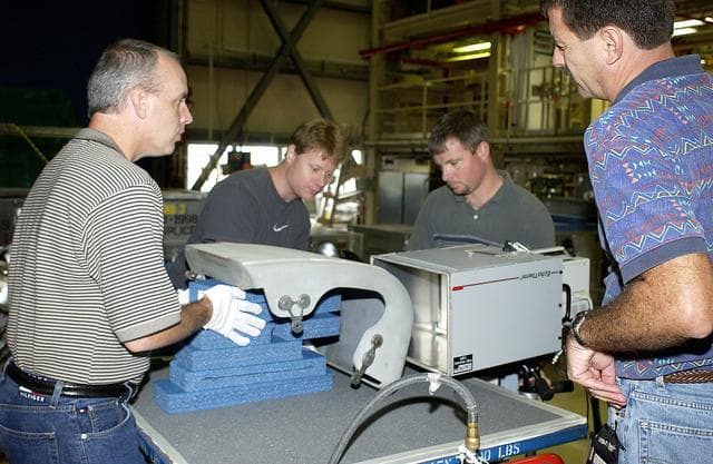 NASA image: KENNEDY SPACE CENTER, FLA. - In the Orbiter Processing Facility, United Space Alliance workers share the task of examining  a Reinforced Carbon Carbon panel using flash thermography.  From left are Dan Kenna, Jim Landy, Paul Ogletree and Dan Phillips.  Attached to the leading edge of the wing of the orbiters,  the gray carbon composite RCC panels have sufficient strength to withstand the aerodynamic forces experienced during launch and reentry, which can reach as high as 800 pounds per square foot.  The operating range of RCC is from minus 250º F to about 3,000º F, the temperature produced by friction with the atmosphere during reentry.