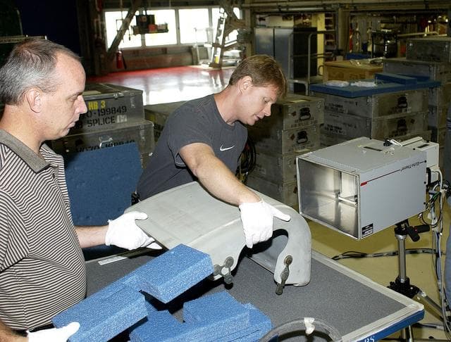 NASA image: KENNEDY SPACE CENTER, FLA. - In the Orbiter Processing Facility, United Space Alliance workers Dan Kenna and Jim Landy prepare to examine a Reinforced Carbon Carbon panel using flash thermography.  Attached to the leading edge of the wing of the orbiters,  the gray carbon composite RCC panels have sufficient strength to withstand the aerodynamic forces experienced during launch and reentry, which can reach as high as 800 pounds per square foot.  The operating range of RCC is from minus 250º F to about 3,000º F, the temperature produced by friction with the atmosphere during reentry.