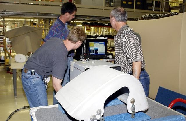NASA image: KENNEDY SPACE CENTER, FLA. - In the Orbiter Processing Facility, United Space Alliance workers Jim Landy (front), Dan Phillips and Dan Kenna watch a monitor showing results of flash thermography on the Reinforced Carbon Carbon panel on the table (foreground).  Attached to the leading edge of the wing of the orbiters,  the gray carbon composite RCC panels have sufficient strength to withstand the aerodynamic forces experienced during launch and reentry, which can reach as high as 800 pounds per square foot.  The operating range of RCC is from minus 250º F to about 3,000º F, the temperature produced by friction with the atmosphere during reentry.