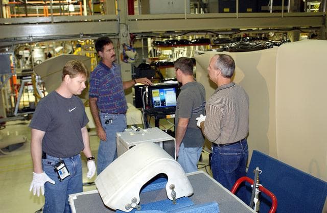 NASA image: KENNEDY SPACE CENTER, FLA. - In the Orbiter Processing Facility, United Space Alliance workers (left to right) Jim Landy, Dan Phillips, Paul Ogletree and Dan Kenna check results of flash thermography on the Reinforced Carbon Carbon panel on the table (foreground).  Attached to the leading edge of the wing of the orbiters,  the gray carbon composite RCC panels have sufficient strength to withstand the aerodynamic forces experienced during launch and reentry, which can reach as high as 800 pounds per square foot.  The operating range of RCC is from minus 250º F to about 3,000º F, the temperature produced by friction with the atmosphere during reentry.