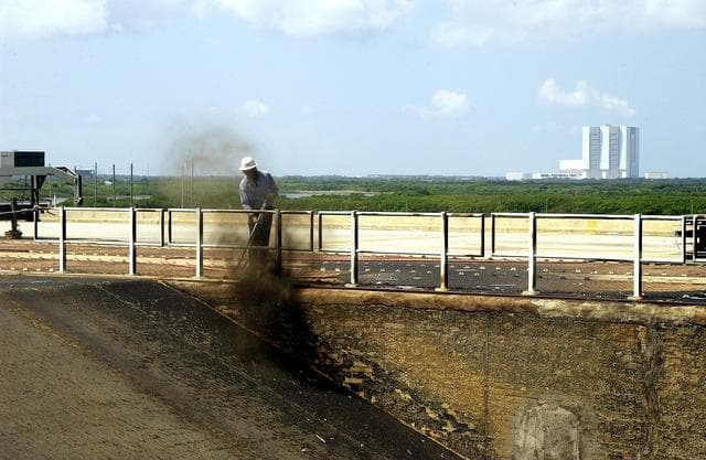 NASA image: KENNEDY SPACE CENTER, FLA. - A worker sandblasts the surface behind the Mobile Launcher Platform on Launch Pad 39A .  Routine maintenance includes sandblasting and repainting as preventive means to minimize corrosion.