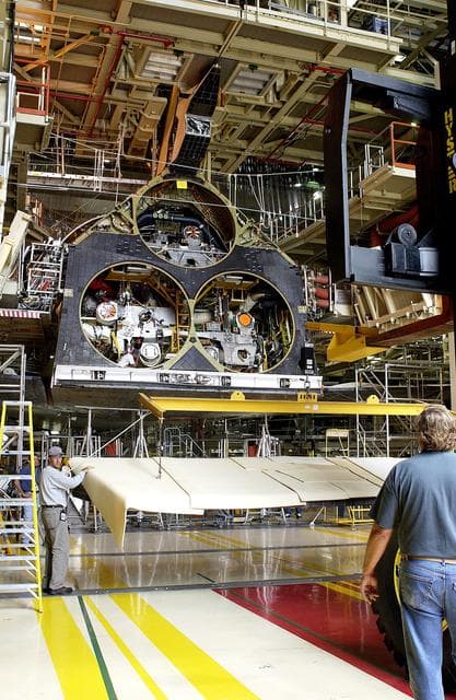 NASA image: KENNEDY SPACE CENTER, FLA. -  Workers in the Orbiter Processing Facility get ready to lift and install the rear body flap on orbiter Discovery.  The body flap, which is temporarily under protective covering, attaches below the main engines.