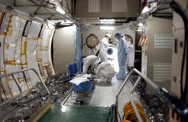 NASA image: KENNEDY SPACE CENTER, FLA. - In the Space Station Processing Facility, Japanese astronaut Koichi Wakata,  dressed in blue protective clothing (at right),  looks at the inside of the Pressurized Module, or PM, part of the Japanese Experiment Module (JEM), along with technicians.  The PM provides a shirt-sleeve environment in which astronauts on the International Space Station can conduct microgravity experiments. There are a total of 23 racks, including 10 experiment racks, inside the PM providing a power supply, communications, air conditioning, hardware cooling, water control and experiment support functions.