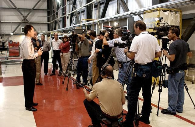 NASA image: KENNEDY SPACE CENTER, FLA. - NASA Vehicle Manager Scott Thurston (left) talks to a phalanx of media in the Orbiter Processing Facility.  The media was invited to see the orbiter Atlantis as it is being prepared for Return to Flight.  Both local and national reporters representing print and TV networks were able to see work in progress on Atlantis, including the reinstallation of the Reinforced Carbon-Carbon panels on the orbiter’s wing leading edge; wiring inspections; and checks of the engines in the Orbital Maneuvering System.