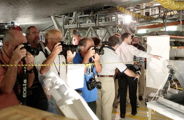 NASA image: KENNEDY SPACE CENTER, FLA. -  In the Orbiter Processing Facility,  while a few photographers (left) set up for photos, NASA Vehicle Manager Scott Thurston (right, with arm extended) talks about the Reinforced Carbon-Carbon panel at right.   The media was invited to see the orbiter Atlantis as it is being prepared for Return to Flight.  Both local and national reporters representing print and TV networks were able to see work in progress on Atlantis, including the reinstallation of the Reinforced Carbon-Carbon panels on the orbiter’s wing leading edge; wiring inspections; and checks of the engines in the Orbital Maneuvering System.