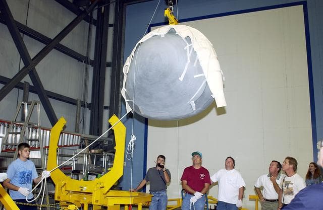 NASA image: KENNEDY SPACE CENTER, FLA. - In the Orbiter Processing Facility, workers watch as the nose cap of the orbiter Atlantis is moved toward the stand at left.  The cap was removed from the orbiter for routine inspection. The nose cap is made of reinforced carbon-carbon (RCC), which has an operating range of minus 250° F to about 3,000° F.