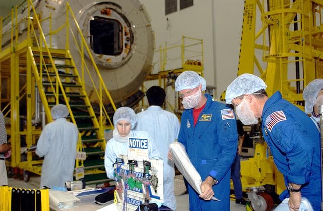 NASA image: KENNEDY SPACE CENTER, FLA. - In the Space Station Processing Facility, STS-115 Mission Specialist Joseph Tanner (left) and STS-117 Mission Specialist James Reilly (right) are donning protective clothing to interface with the Japanese Experiment Module (JEM), in the background.  Equipment familiarization is a routine part of astronaut training and launch preparations.