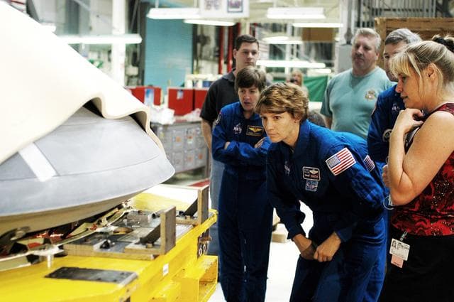 NASA image: KENNEDY SPACE CENTER, FLA. -  In the Orbiter Processing Facility, STS-114 crew members look at the nose cap recently removed from Atlantis.  From left are Mission Specialist Wendy Lawrence, Commander Eileen Collins and Pilot James Kelly (behind Collins).  Lawrence is a new addition to the mission crew.  The STS-114 crew is at KSC to take part in crew equipment and orbiter familiarization.