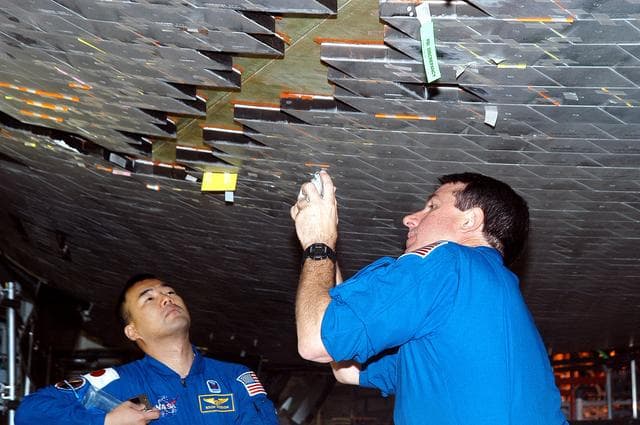 NASA image: KENNEDY SPACE CENTER, FLA. -  In the Orbiter Processing Facility, STS-114 Mission Specialists Soichi Noguchi and Stephen Robinson take a close look at the some of the tiles underneath Atlantis.  Noguchi is with the Japan Aerospace Exploration Agency, JAXA.  The STS-114 crew is at KSC to take part in crew equipment and orbiter familiarization.