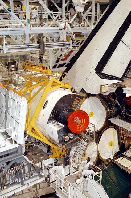 NASA image: KENNEDY SPACE CENTER, FLA. - In the Orbiter Processing Facility, an orbital maneuvering system (OMS) pod is moved into place on Atlantis.  It is one of two OMS pods attached to the upper aft fuselage left and right sides. Fabricated primarily of graphite epoxy composite and aluminum, each pod is 21.8 feet long and 11.37 feet wide at its aft end and 8.41 feet wide at its forward end, with a surface area of approximately 435 square feet. Each pod houses the Reaction Control System propulsion components used for inflight maneuvering and is attached to the aft fuselage with 11 bolts.