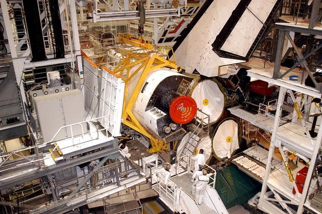 NASA image: KENNEDY SPACE CENTER, FLA. - In the Orbiter Processing Facility, an orbital maneuvering system (OMS) pod is moved into place on Atlantis.  It is one of two OMS pods attached to the upper aft fuselage left and right sides. Fabricated primarily of graphite epoxy composite and aluminum, each pod is 21.8 feet long and 11.37 feet wide at its aft end and 8.41 feet wide at its forward end, with a surface area of approximately 435 square feet. Each pod houses the Reaction Control System propulsion components used for inflight maneuvering and is attached to the aft fuselage with 11 bolts.