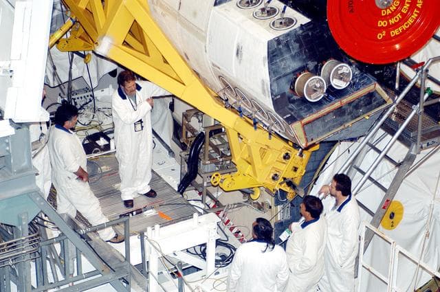 NASA image: KENNEDY SPACE CENTER, FLA. - In the Orbiter Processing Facility, technicians move an orbital maneuvering system (OMS) pod into the correct position on Atlantis. The OMS pod is one of two that are attached to the upper aft fuselage left and right sides. Fabricated primarily of graphite epoxy composite and aluminum, each pod is 21.8 feet long and 11.37 feet wide at its aft end and 8.41 feet wide at its forward end, with a surface area of approximately 435 square feet. Each pod houses the Reaction Control System propulsion components used for inflight maneuvering and is attached to the aft fuselage with 11 bolts.