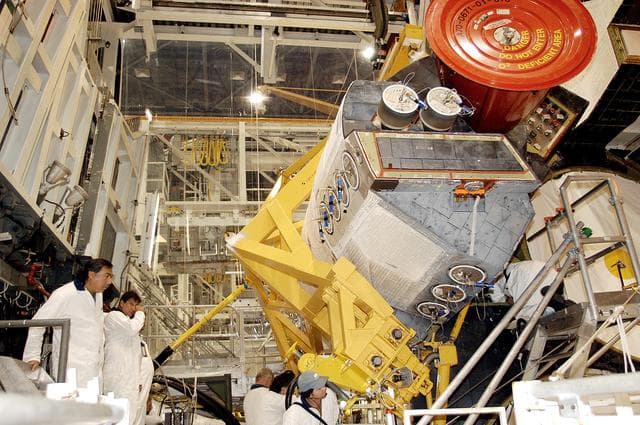 NASA image: KENNEDY SPACE CENTER, FLA. - In the Orbiter Processing Facility, technicians make final adjustments to the orbital maneuvering system (OMS) pod being installed on Atlantis.   The OMS pod is one of two that are attached to the upper aft fuselage left and right sides. Fabricated primarily of graphite epoxy composite and aluminum, each pod is 21.8 feet long and 11.37 feet wide at its aft end and 8.41 feet wide at its forward end, with a surface area of approximately 435 square feet. Each pod houses the Reaction Control System propulsion components used for inflight maneuvering and is attached to the aft fuselage with 11 bolts.