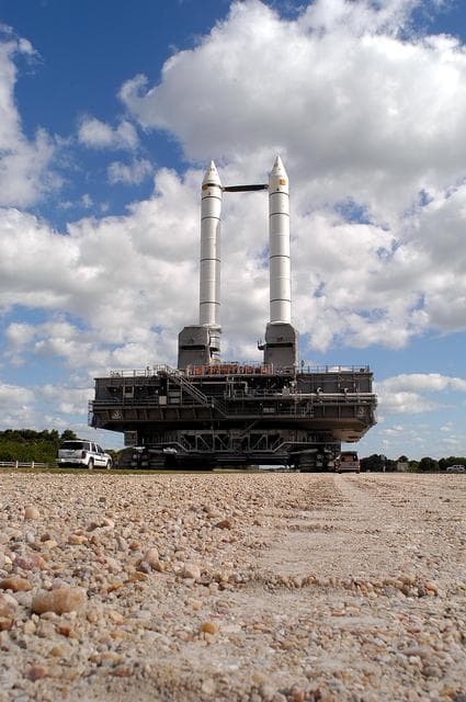 NASA image: KENNEDY SPACE CENTER, FLA. -  Mobile Launcher Platform (MLP) number 3 and a set of twin solid rocket boosters, atop the crawler-transporter, inch along the crawlerway in support of the second engineering analysis vibration test on the crawler and MLP. The view reveals the river gravel surface that is 4 inches thick on the straightaway sections and 8 inches thick on curves. The crawler is moving at various speeds up to 1 mph in an effort to achieve vibration data gathering goals as it leaves the VAB, travels toward Launch Pad 39A and then returns.  The boosters are braced at the top for stability.  The primary purpose of these rollout tests is to gather data to develop future maintenance requirements on the transport equipment and the flight hardware. Various parts of the MLP and crawler transporter have been instrumented with vibration data collection equipment.