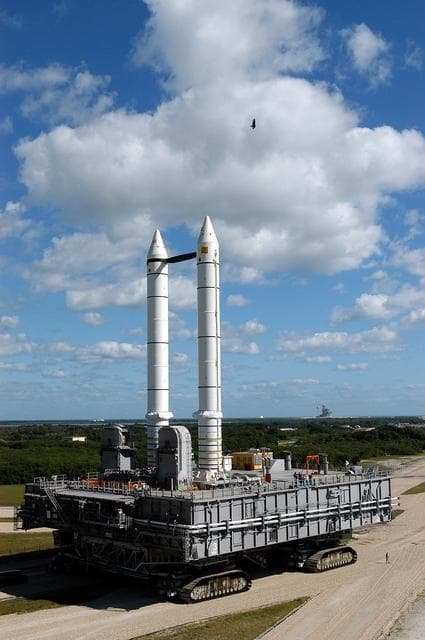 NASA image: KENNEDY SPACE CENTER, FLA. -  A high-flying bird takes a closer look at the Mobile Launcher Platform (MLP) number 3 with twin solid rocket boosters bolted to it as it crawls toward Launch Pad 39A, in the background.  The crawler is moving along the crawlerway at various speeds up to 1 mph in an effort to achieve vibration data gathering goals as it travels toward Launch Pad 39A and then returns.  The boosters are braced at the top for stability.  The primary purpose of these rollout tests is to gather data to develop future maintenance requirements on the transport equipment and the flight hardware. Various parts of the MLP and crawler transporter have been instrumented with vibration data collection equipment.