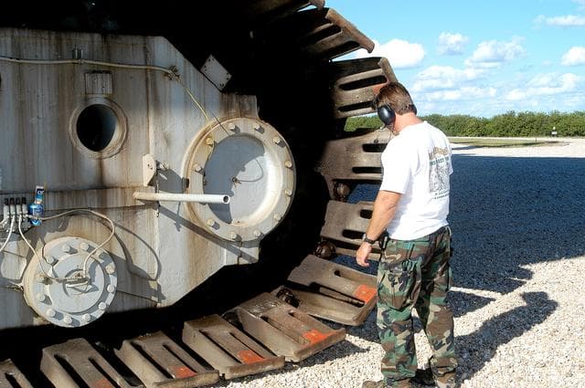 NASA image: KENNEDY SPACE CENTER, FLA. - A Kennedy Space Center technician inspects the shoes on one of eight tracks of a crawler-transporter (CT).  The CT is moving Mobile Launcher Platform (MLP) number 3 with a set of twin solid rocket boosters bolted on top to the intersection in the crawlerway in support of the second engineering analysis vibration test on the crawler and MLP.  The crawler is moving at various speeds up to 1 mph in an effort to achieve vibration data gathering goals as it leaves the VAB, travels toward Launch Pad 39A and then returns. The boosters are braced at the top for stability. The primary purpose of these rollout tests is to gather data to develop future maintenance requirements on the transport equipment and the flight hardware. Various parts of the MLP and crawler transporter have been instrumented with vibration data collection equipment.