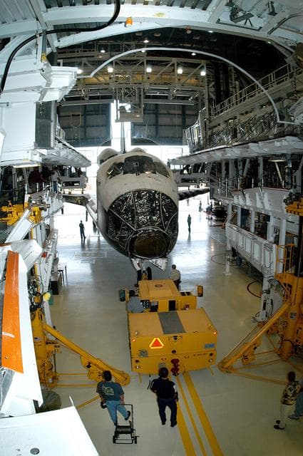 NASA image: KENNEDY SPACE CENTER, FLA. - Workers prepare to tow the Space Shuttle orbiter Atlantis from the Orbiter Processing Facility (OPF) to the Vehicle Assembly Building (VAB). The move will allow work to be performed in the OPF that can only be accomplished while the bay is empty. Work scheduled in the processing facility includes annual validation of the bay's cranes, work platforms, lifting mechanisms, and jack stands. Atlantis will remain in the VAB for about 10 days, then return to the OPF as work resumes to prepare it for launch in September 2004 on the first return-to-flight mission, STS-114.