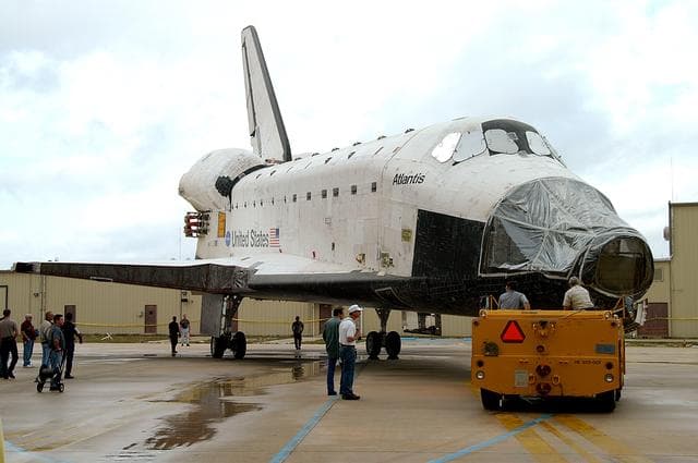 NASA image: KENNEDY SPACE CENTER, FLA. - The Space Shuttle orbiter Atlantis is turned into position outside the Orbiter Processing Facility (OPF) for its tow to the Vehicle Assembly Building (VAB). The move will allow work to be performed in the OPF that can only be accomplished while the bay is empty. Work scheduled in the processing facility includes annual validation of the bay's cranes, work platforms, lifting mechanisms, and jack stands. Atlantis will remain in the VAB for about 10 days, then return to the OPF as work resumes to prepare it for launch in September 2004 on the first return-to-flight mission, STS-114.