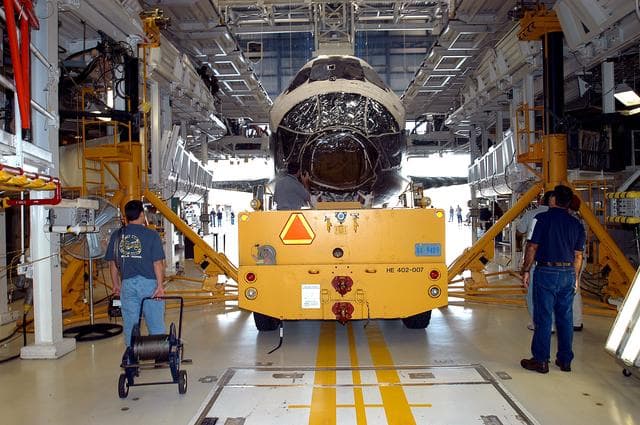 NASA image: KENNEDY SPACE CENTER, FLA. - Workers back the Space Shuttle orbiter Atlantis out of the Orbiter Processing Facility (OPF) for its move to the Vehicle Assembly Building (VAB). The move will allow work to be performed in the OPF that can only be accomplished while the bay is empty. Work scheduled in the processing facility includes annual validation of the bay's cranes, work platforms, lifting mechanisms, and jack stands. Atlantis will remain in the VAB for about 10 days, then return to the OPF as work resumes to prepare it for launch in September 2004 on the first return-to-flight mission, STS-114.