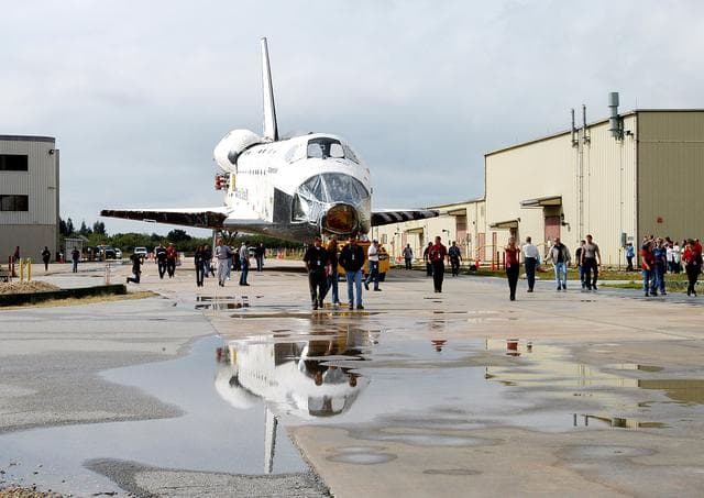 NASA image: KENNEDY SPACE CENTER, FLA. - The Space Shuttle orbiter Atlantis is reflected in a rain puddle as it is towed from the Orbiter Processing Facility (OPF) to the Vehicle Assembly Building (VAB). The move will allow work to be performed in the OPF that can only be accomplished while the bay is empty. Work scheduled in the processing facility includes annual validation of the bay's cranes, work platforms, lifting mechanisms, and jack stands. Atlantis will remain in the VAB for about 10 days, then return to the OPF as work resumes to prepare it for launch in September 2004 on the first return-to-flight mission, STS-114.