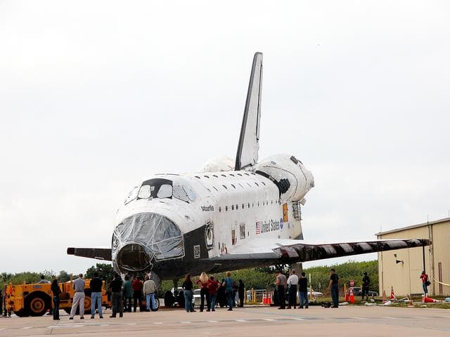NASA image: KENNEDY SPACE CENTER, FLA. - Workers walk with Space Shuttle orbiter Atlantis from the Orbiter Processing Facility (OPF) to the Vehicle Assembly Building (VAB) high bay 4. The move will allow work to be performed in the OPF that can only be accomplished while the bay is empty. Work scheduled in the processing facility includes annual validation of the bay's cranes, work platforms, lifting mechanisms, and jack stands. Atlantis will remain in the VAB for about 10 days, then return to the OPF as work resumes to prepare it for launch in September 2004 on the first return-to-flight mission, STS-114.
