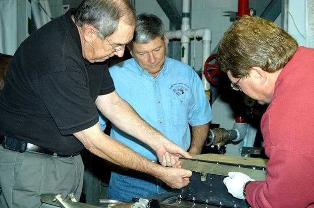 NASA image: KENNEDY SPACE CENTER, FLA. -- United Space Alliance (USA) Vice President and Space Shuttle Program Manager Howard DeCastro (left) and NASA Deputy Associate Administrator for Space Station and Shuttle Programs Michael Kostelnik (center) are briefed on the use of a cold plate in Orbiter Processing Facility Bay 2 by a USA technician (right).  NASA and USA Space Shuttle program management are participating in a leadership workday.  The day is intended to provide management with an in-depth, hands-on look at Shuttle processing activities at KSC.
