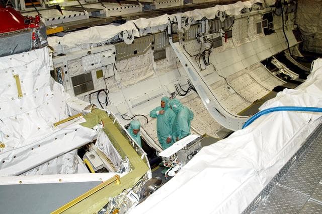 NASA image: KENNEDY SPACE CENTER, FLA. -- In Orbiter Processing Facility Bay 1, NASA Deputy Associate Administrator for Space Station and Shuttle Programs Michael Kostelnik (left) and United Space Alliance (USA) Vice President and Space Shuttle Program Manager Howard DeCastro (right) are briefed by a USA technician (center) on Shuttle processing in the payload bay of orbiter Atlantis.  NASA and USA Space Shuttle program management are participating in a leadership workday.  The day is intended to provide management with an in-depth, hands-on look at Shuttle processing activities at KSC.
