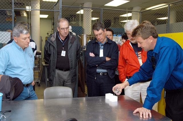 NASA image: KENNEDY SPACE CENTER, FLA. -- From left, NASA Deputy Associate Administrator for Space Station and Shuttle Programs Michael Kostelnik and United Space Alliance (USA) Vice President and Space Shuttle Program Manager Howard DeCastro are briefed on the properties of the tile used in the Shuttle's Thermal Protection System (TPS) by USA Manager of the TPS Facility Martin Wilson (right).  NASA and USA Space Shuttle program management are participating in a leadership workday.  The day is intended to provide management with an in-depth, hands-on look at Shuttle processing activities at KSC.