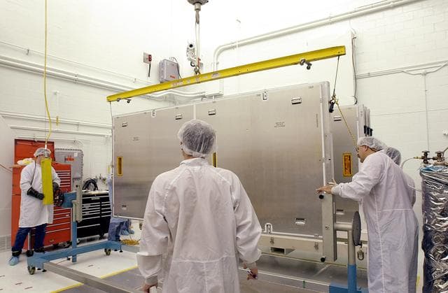NASA image: VANDENBERG AFB, CALIF. - Workers in the NASA spacecraft processing facility on North Vandenberg Air Force Base prepare to rotate the framework containing one of four solar panels to be installed on the Gravity Probe B spacecraft.  Installing each array is a 3-day process and includes a functional deployment test.  The Gravity Probe B mission is a relativity experiment developed by NASA’s Marshall Space Flight Center, Stanford University and Lockheed Martin.  The spacecraft will test two extraordinary predictions of Albert Einstein’s general theory of relativity that he advanced in 1916: the geodetic effect (how space and time are warped by the presence of the Earth) and frame dragging (how Earth’s rotation drags space and time around with it).  Gravity Probe B consists of four sophisticated gyroscopes that will provide an almost perfect space-time reference system.  The mission will look in a precision manner for tiny changes in the direction of spin.
