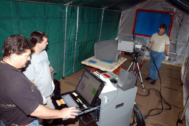 NASA image: KENNEDY SPACE CENTER, FLA. -  Dan Phillips (left) and Donald Nielen, with United Space Alliance, watch a monitor as  Jim Landy, NDE specialist with USA, prepares to examine a Reinforced Carbon Carbon panel (on the table, center) using flash thermography.  A relatively new procedure at KSC, thermography uses high intensity light to heat areas of the panels. The panels are then immediately scanned with an infrared camera. As the panels cool, any internal flaws are revealed. The gray carbon composite RCC panels are attached to the leading edge of the wing of the orbiters.  They have sufficient strength to withstand the aerodynamic forces experienced during launch and reentry, which can reach as high as 800 pounds per square foot.  The operating range of RCC is from minus 250º F to about 3,000º F, the temperature produced by friction with the atmosphere during reentry.  The panels will be installed on the orbiter Discovery, designated  for the first Return to Flight mission, STS-114.