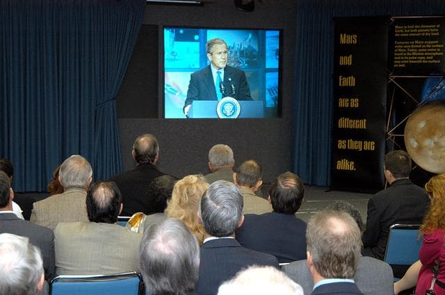 NASA image: KENNEDY SPACE CENTER, FLA. -- KSC management and other employees gather in the Center’s television studio to watch the address by President George W. Bush at NASA Headquarters in Washington, D.C., stating his goals for NASA’s new mission:  Completing the International Space Station, retiring the Space Shuttle orbiters, developing a new crew exploration vehicle, and returning to the moon and beyond within the next two decades.   Pres. Bush was welcomed by NASA Administrator Sean O’Keefe and Expedition 8 Commander Michael Foale, who greeted him from the International Space Station.  Members of the Washington, D.C., audience included astronauts Eileen Collins, Ed Lu and Michael Lopez-Alegria, and former astronaut Gene Cernan.