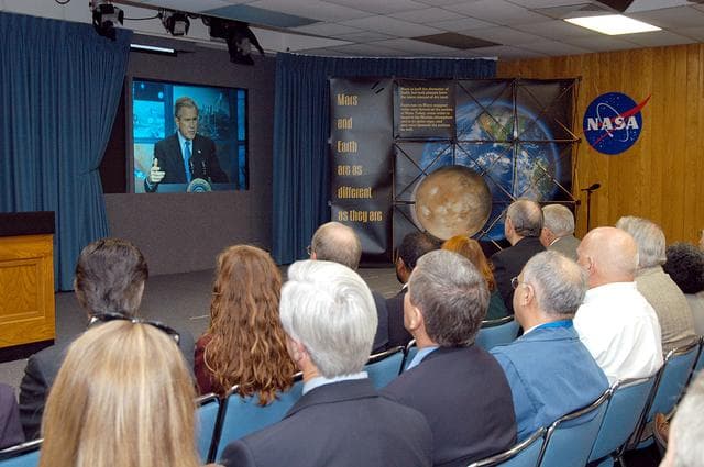 NASA image: KENNEDY SPACE CENTER, FLA. -- KSC management and other employees gather in the Center’s television studio to watch the address by President George W. Bush from NASA Headquarters stating his goals for NASA’s new mission.  Seated in the front row, left to right, are Ken Aguilar, chief, Equal Opportunity office; Lisa Malone, director of External Affairs; Bruce Buckingham, assistant to Dr. Woodrow Whitlow, KSC deputy director; Dr. Whitlow; Shannon Roberts, with External Affairs; Howard DeCastro, vice president and Space Shuttle program manager, United Space Alliance; and Bill Pickavance vice president and associate program manager of Florida Operations, USA.  The President’s goals are completing the International Space Station, retiring the Space Shuttle orbiters, developing a new crew exploration vehicle, and returning to the moon and beyond within the next two decades. Pres. Bush was welcomed by NASA Administrator Sean O’Keefe and Expedition 8 Commander Michael Foale, who greeted him from the International Space Station.  Members of the Washington, D.C., audience included astronauts Eileen Collins, Ed Lu and Michael Lopez-Alegria, and former astronaut Gene Cernan.