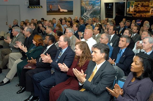 NASA image: KENNEDY SPACE CENTER, FLA. -- In the KSC television studio, KSC management and other employees applaud President George W. Bush, who addressed the public and an assembly of government officials at NASA Headquarters as he outlined a new focus and vision for the space agency.  Seated in the front row, left to right, are Bill Pickavance vice president and associate program manager of Florida Operations, United Space Alliance (USA) ; Howard DeCastro, vice president and Space Shuttle program manager, USA; Shannon Roberts, with External Affairs; Woodrow Whitlow, KSC deputy director; Bruce Buckingham, assistant to Dr. Whitlow; Lisa Malone, director of External Affairs; Ken Aguilar, chief, Equal Opportunity office; and Cheryl Cox, External Affairs.  The President stated his goals for NASA’s new mission: Completing the International Space Station, retiring the Space Shuttle orbiters, developing a new crew exploration vehicle, and returning to the moon and beyond within the next two decades.   Pres. Bush was welcomed by NASA Administrator Sean O’Keefe and Expedition 8 Commander Michael Foale, who greeted him from the International Space Station.  Members of the Washington, D.C., audience included astronauts Eileen Collins, Ed Lu and Michael Lopez-Alegria, and former astronaut Gene Cernan.