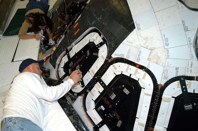 NASA image: KENNEDY SPACE CENTER, FLA. -- Les Hanks (foreground) and Darlene Beville (background), with United Space Alliance,  prepare a window on Atlantis for removal.  The windows are being removed to inspect them for contaminants in the thermal seal.  Atlantis has been undergoing routine maintenance in the Orbiter Processing Facility for Return to Flight, on mission STS-114.