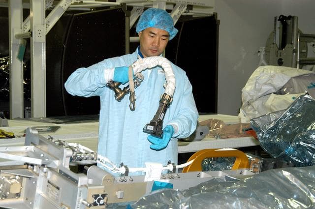 NASA image: KENNEDY SPACE CENTER, FLA. -  Dressed in protective suits, STS-114 Mission Specialist Soichi Noguchi, with the Japanese Aerospace Exploration Agency (JAXA), handles equipment that will be used on the mission.  He and other crew members are at KSC for equipment familiarization.  STS-114 is classified as Logistics Flight 1 to the International Space Station, delivering new supplies and replacing one of the orbital outpost’s Control Moment Gyroscopes (CMGs). STS-114 will also carry a Raffaello Multi-Purpose Logistics Module and the External Stowage Platform-2.  The crew is slated to conduct at least three spacewalks: They will demonstrate repair techniques of the Shuttle’s Thermal Protection System,  replace the failed CMG with one delivered by the Shuttle, and  install the External Stowage Platform.