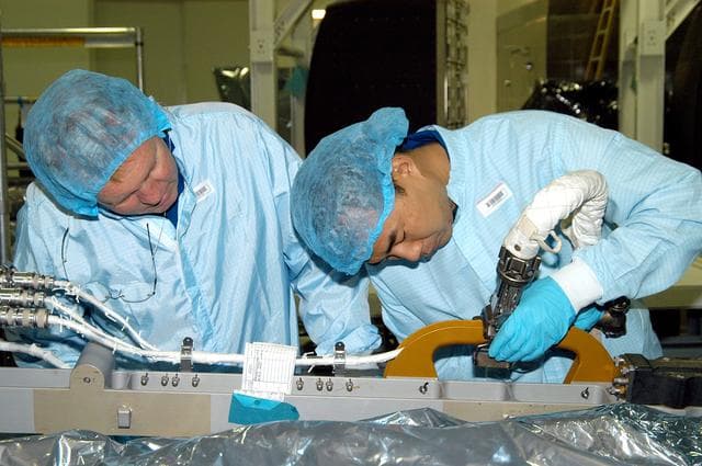 NASA image: KENNEDY SPACE CENTER, FLA. -  Dressed in protective suits, STS-114 Mission Specialist Andrew Thomas (left) and Soichi Noguchi, who is with the Japanese Aerospace Exploration Agency (JAXA), handle equipment in the Space Station Processing Facility that will be used on the mission.  They and other crew members are at KSC for equipment familiarization.  STS-114 is classified as Logistics Flight 1 to the International Space Station, delivering new supplies and replacing one of the orbital outpost’s Control Moment Gyroscopes (CMGs). STS-114 will also carry a Raffaello Multi-Purpose Logistics Module and the External Stowage Platform-2.  The crew is slated to conduct at least three spacewalks: They will demonstrate repair techniques of the Shuttle’s Thermal Protection System,  replace the failed CMG with one delivered by the Shuttle, and  install the External Stowage Platform.